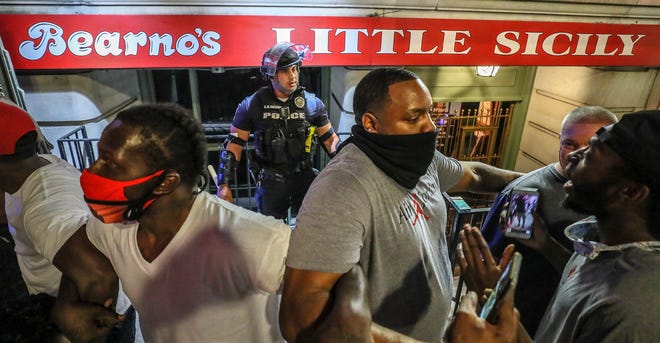 Five men, including Christopher Gales, Darren Lee Jr, Ricky McClellan and Julian "New Heightz" De La Cruz linked arms to keep a crowd of protesters away from LMPD officer Galen Hinshaw on the first night of protests in Louisville on May 28, 2020.