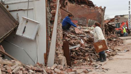 Shawna Driscoll cries as she hands unbroken ceramic plates to her friend Angee Wilson while digging through debris at Wilson&#39;s mother&#39;s tax office in Mayfield on December 15.